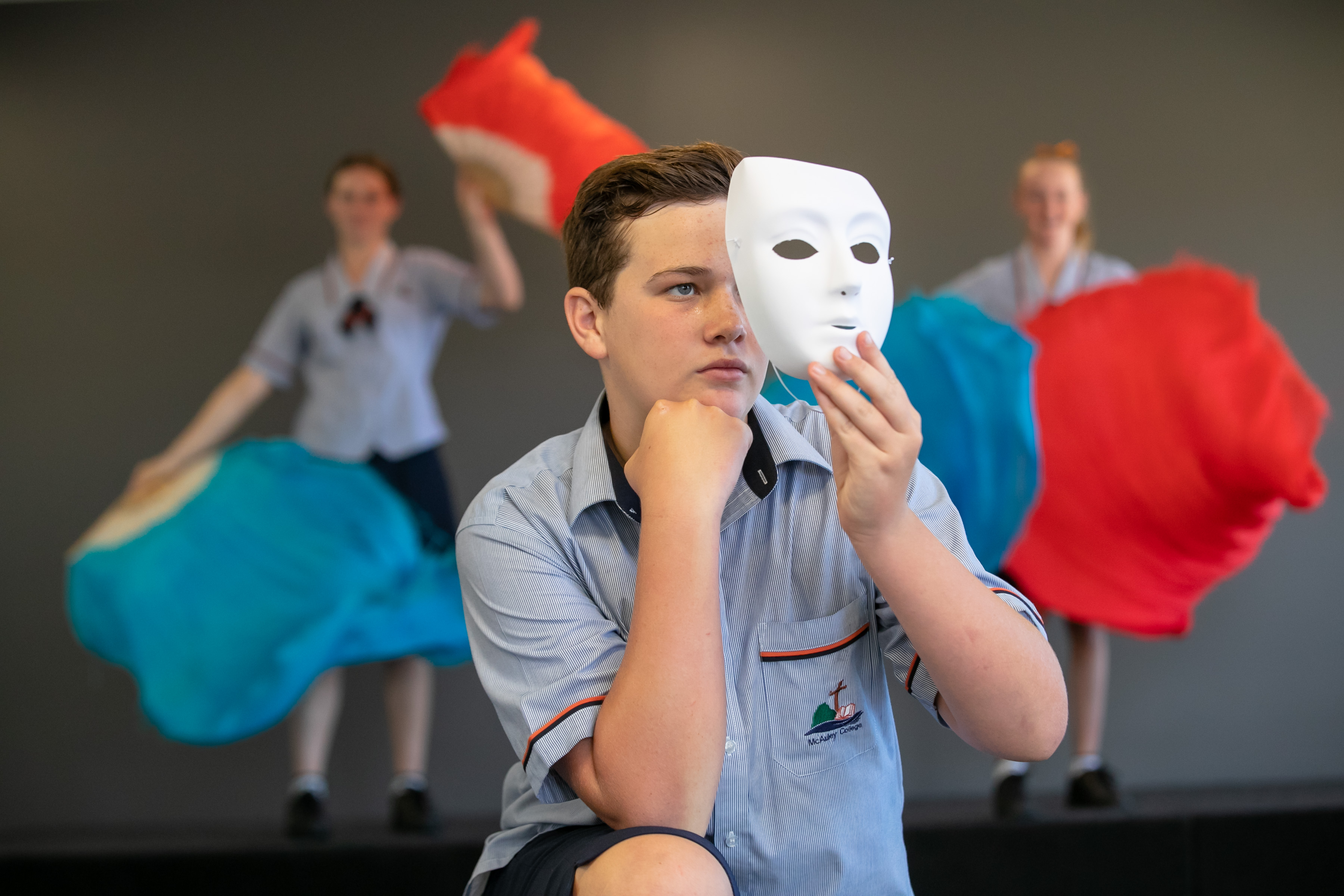 Drama student holding a mask. There are two students behind him, waving flags.
