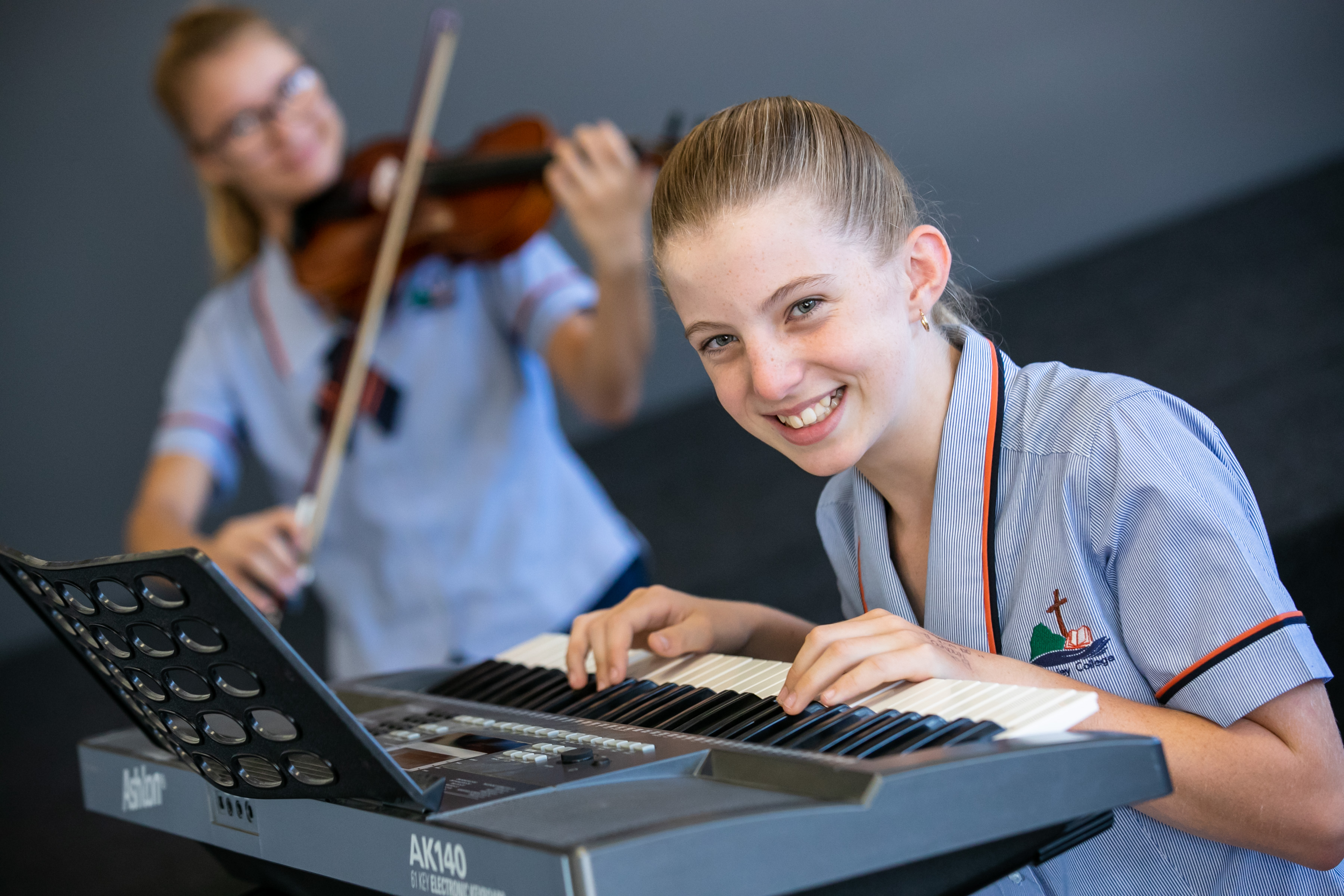 A student playing the keyboard and a student playing the violin is in the background behind her.